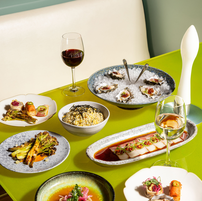 Elegant table spread with oysters on ice, grilled vegetables, seafood dishes, and wine glasses on a bright green tablecloth