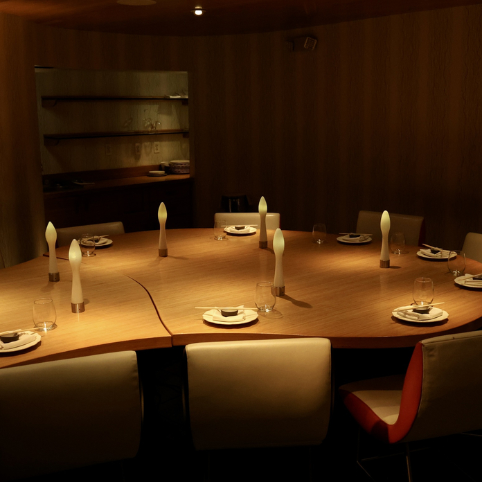 Intimate dining room with round wooden table set for eight, illuminated candles, and dark wood paneled walls