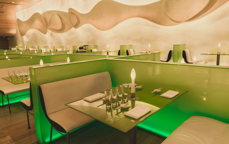 Modern restaurant interior with curved beige ceiling, green booth seating, glass tables, and candle-style lighting throughout