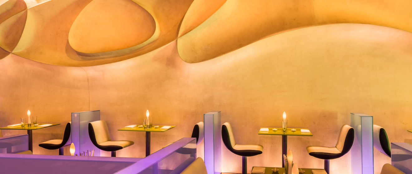 Modern dining area with curved pastel walls, minimalist tables, and contemporary chairs.