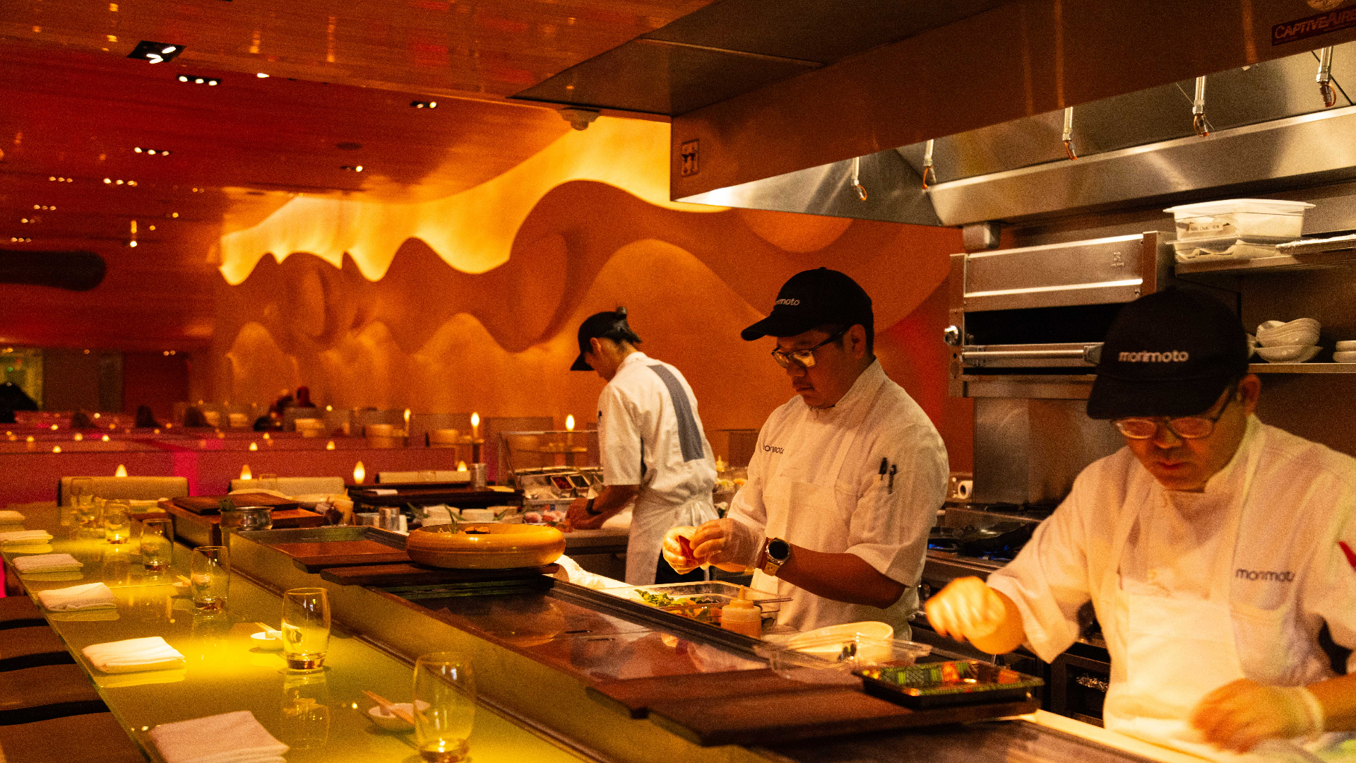 Modern restaurant with green-lit booths, light-colored curved benches, and abstract mural on the wall.