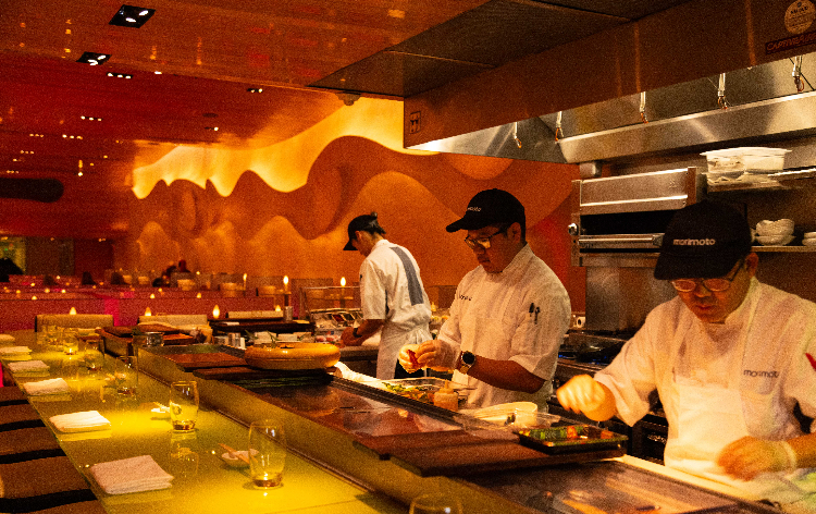Modern restaurant interior with curved beige ceiling, green booth seating, glass tables, and candle-style lighting throughout